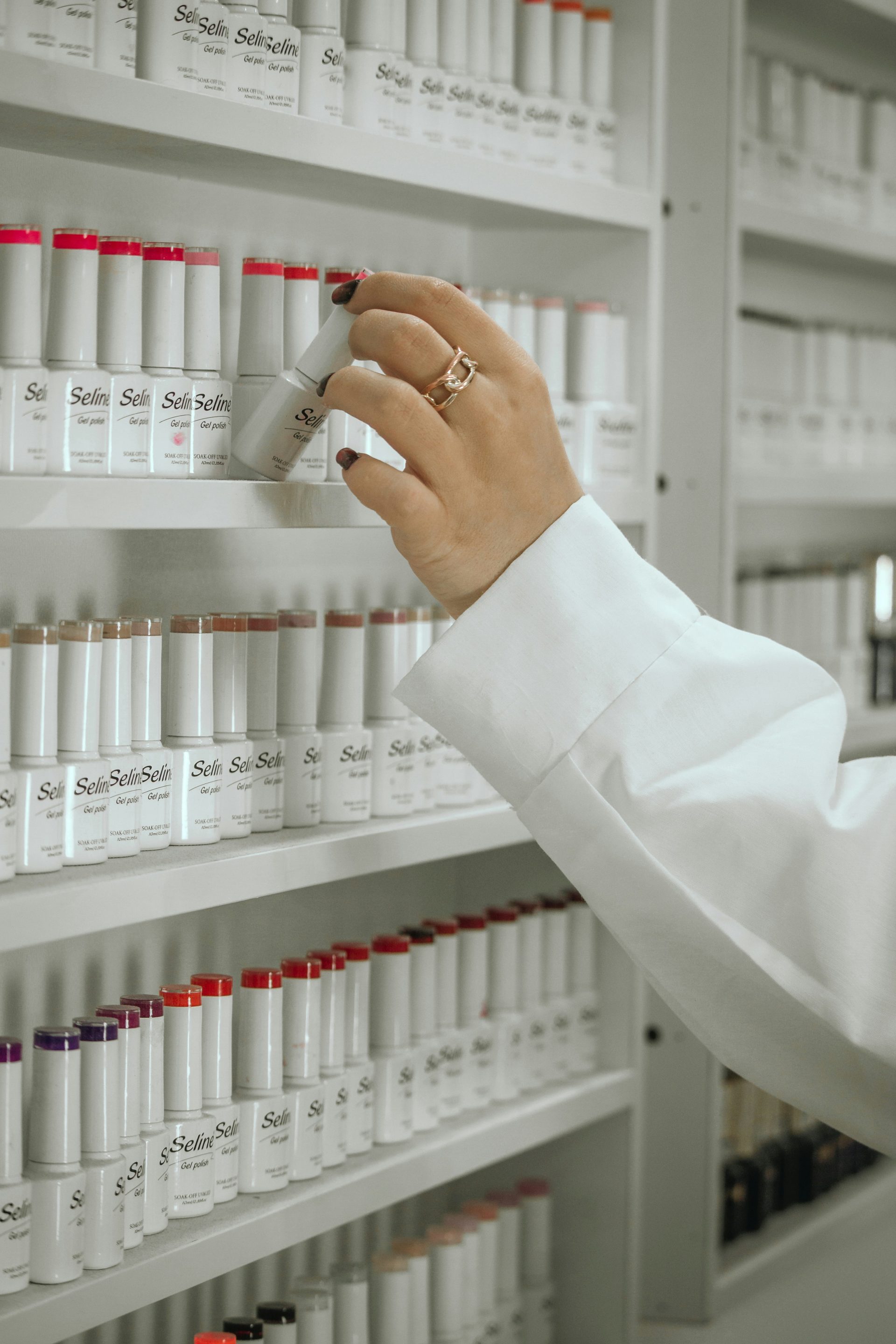A woman in a white lab coat is looking at a shelf of bottles